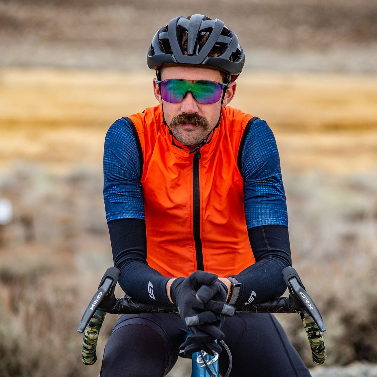 Gravel cyclist wearing orange vest and arm warmers