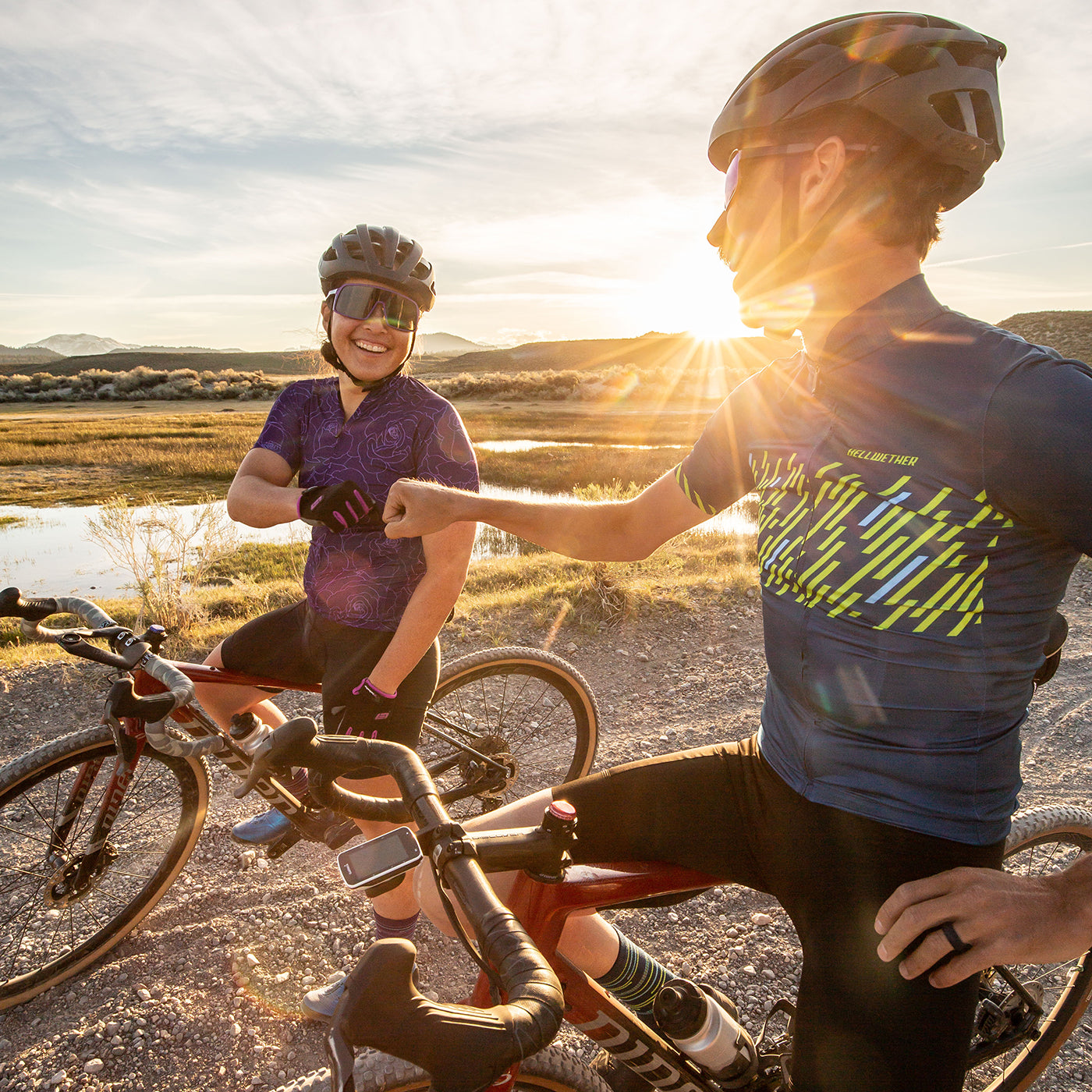 Male and female gravel cyclists fist bump after gravel ride as the sun is setting